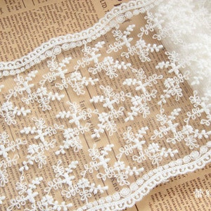May include: White lace trim featuring a floral snowflake design. The delicate trim has a scalloped edge and is ideal for adding a decorative touch to garments or crafts.