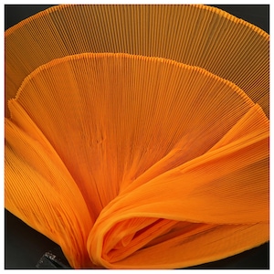 Peut inclure: Un tissu plissé orange vif. Le tissu est plié en forme d'éventail, créant un effet texturé et superposé.