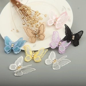 Könnte beinhalten: Sortiment von sieben bunten Schmetterlingsapplikationen mit Strasssteinen. Die Schmetterlinge sind aus durchsichtigem Stoff gefertigt und eignen sich perfekt, um Bastelarbeiten und Projekten einen Hauch von Verspieltheit zu verleihen.