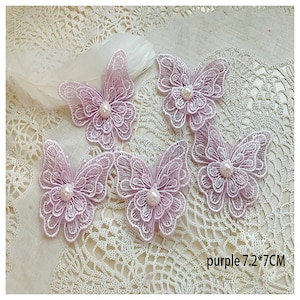 Pode incluir: Cinco aplicações de borboleta de renda roxa com centros de pérolas. Cada aplicação mede 7,2 por 7 centímetros.