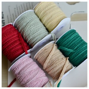 Pu&ograve; includere: Sei bobine di passamaneria arricciata in vari colori, tra cui rosso, verde, beige, rosa e verde chiaro. La passamaneria &egrave; avvolta attorno a bobine bianche.