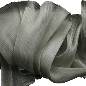 Puede incluir: Una tela gris claro transparente con un fino patrón de rayas verticales. El material está drapeado en pliegues suaves y fluidos, mostrando su calidad translúcida y su superficie delicadamente texturizada con bordes deshilachados visibles.