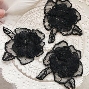 May include: Three black lace flower appliques featuring a delicate floral design. The appliques are ideal for adding a touch of elegance to any project.