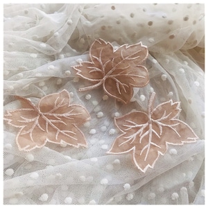 May include: Three beige lace leaf appliques on a white dotted mesh fabric.