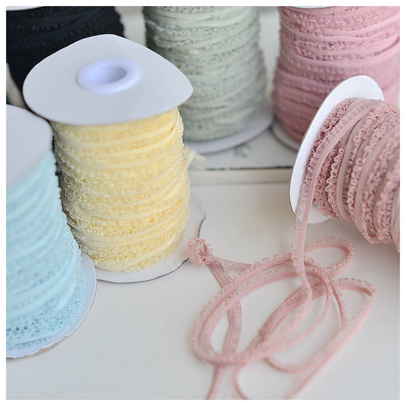 May include: Four spools of lace trim in different colors: black, light green, yellow, and pink. The lace trim is ruffled and has a delicate texture.
