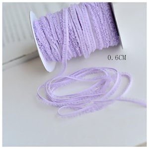 May include: A spool of lavender-colored lace trim with a ruffled edge. The trim is 0.6 centimeters wide.