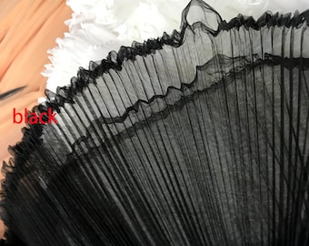 May include: Black pleated tulle fabric with a soft, delicate texture. The fabric is gathered and folded to create a fan-like shape.