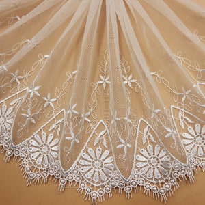 May include: White embroidered lace trim with a scalloped edge and floral design. The lace is delicate and sheer, perfect for adding a touch of elegance to any project.