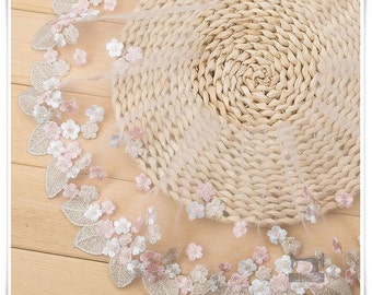 May include: A delicate, white lace trim with pink and silver embroidered flowers and leaves. The trim is shown on a woven straw background.