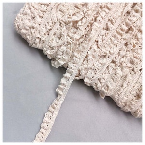 Op de afbeelding: Crèmekleurige gehaakte kantbies met een gegolfde rand.