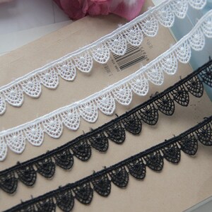 May include: Three pieces of white and black lace trim with scalloped edges. The lace trim is delicate and intricate.