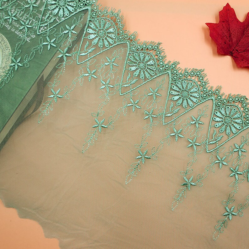 May include: Green lace trim with a scalloped edge and floral embroidery. The lace has a delicate, airy feel and would be perfect for adding a touch of elegance to any project.