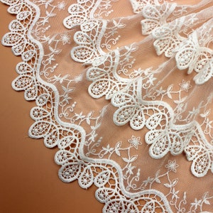 May include: White lace trim with a scalloped edge and floral design. The lace is delicate and intricate, with a soft, flowing texture.