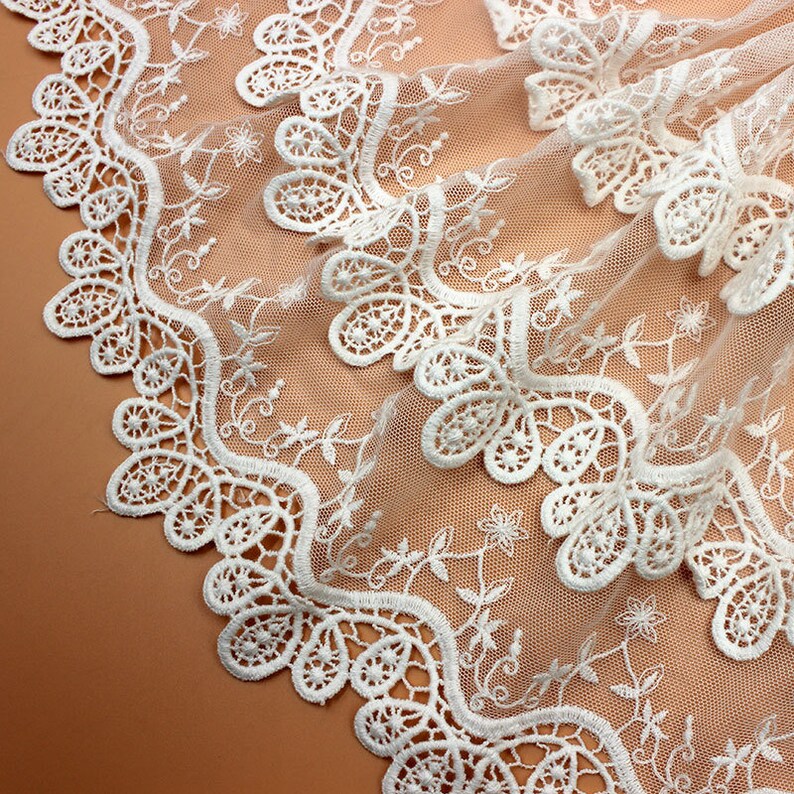May include: White lace trim with a scalloped edge and floral design. The lace is delicate and intricate, with a soft, flowing texture.