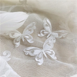 Peut inclure: Trois appliques de papillon en dentelle blanche sur un fond de tissu en maille blanche.