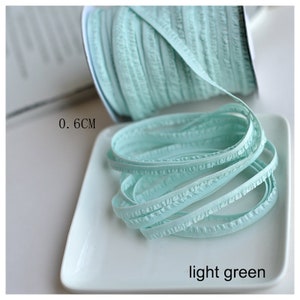 Pu&ograve; includere: Un rotolo di passamaneria verde chiaro con volant, largo 0,6 cm, su un piatto bianco.