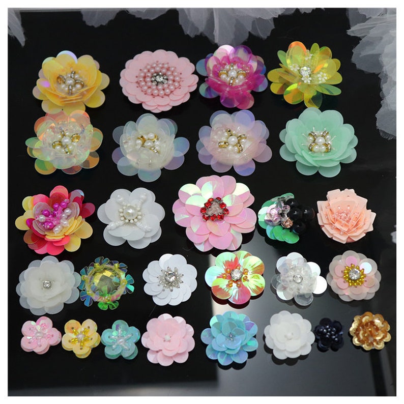 May include: A collection of twenty-five decorative flower appliques in various colors and sizes. Each flower is crafted from layered sequins and features a central embellishment of faux pearls, clear crystals, or metallic beads in a variety of floral shapes.