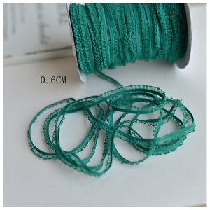 May include: A spool of emerald green ruffled trim with a 0.6 cm width. The trim is made of a sheer fabric with a delicate ruffle edge.