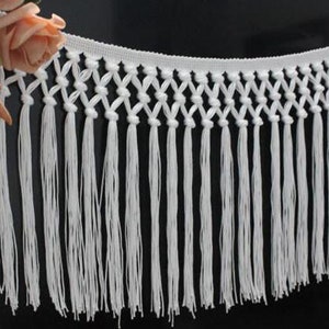 Op de afbeelding: Witte katoenen franje trim met een geknoopt ontwerp. De franje is ongeveer 5 cm lang.
