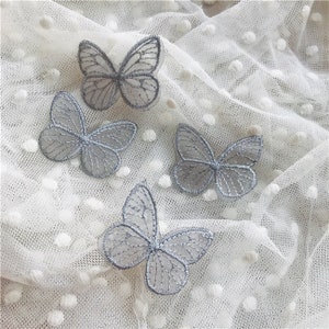 Peut inclure: Quatre appliques de papillon en dentelle grise sur un fond de tissu en maille à pois blancs.