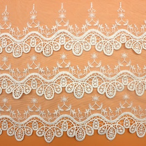 May include: White lace trim with a delicate floral pattern. The trim has a scalloped edge and is perfect for adding a touch of elegance to any project.