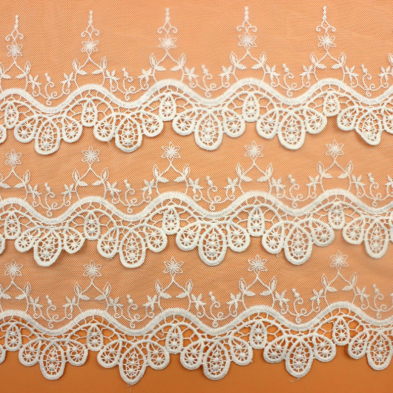 May include: White lace trim with a delicate floral pattern. The trim has a scalloped edge and is perfect for adding a touch of elegance to any project.