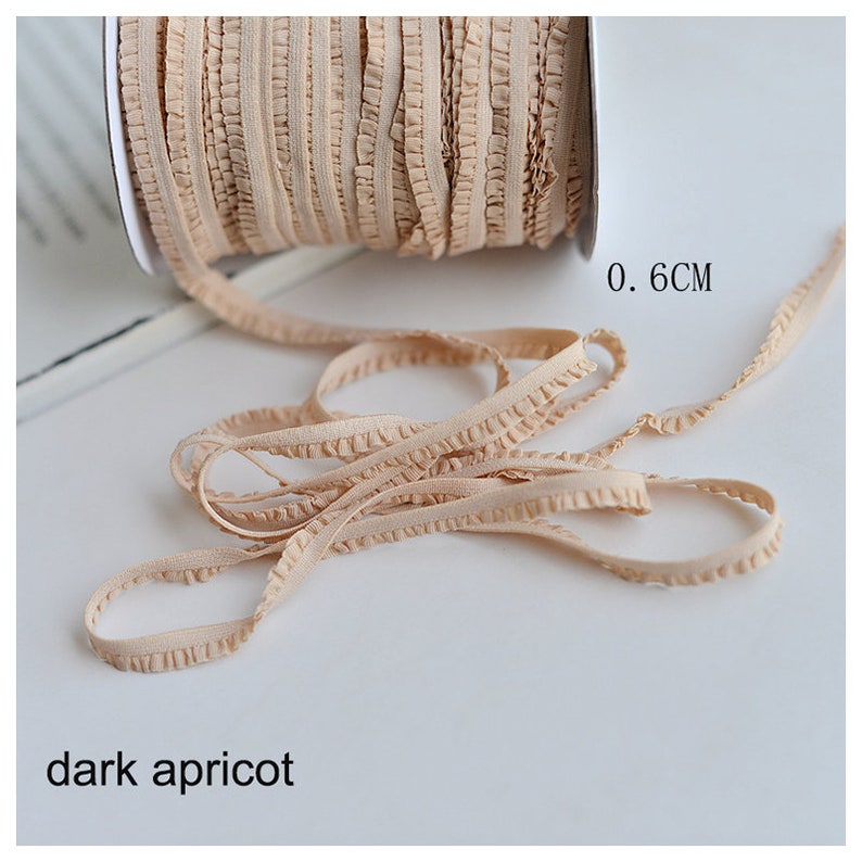 Pu&ograve; includere: Un rotolo di passamaneria elastica con volant di colore albicocca scuro, largo 0,6 cm.