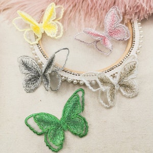 May include: Five embroidered butterfly appliques in various colors, including yellow, pink, silver, green, and white. The butterflies are on a white fabric background.