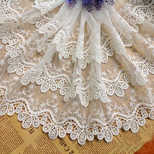 May include: White lace trim with a scalloped edge and delicate floral embroidery. The lace is layered and has a soft, airy feel.