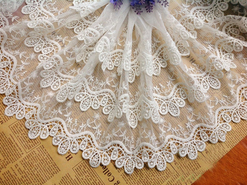 May include: White lace trim with a scalloped edge and delicate floral embroidery. The lace is layered and has a soft, airy feel.