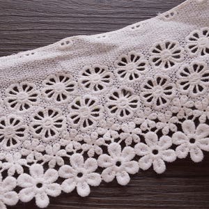 May include: White lace trim with a delicate floral pattern. The lace has a scalloped edge and is perfect for adding a touch of elegance to any project.