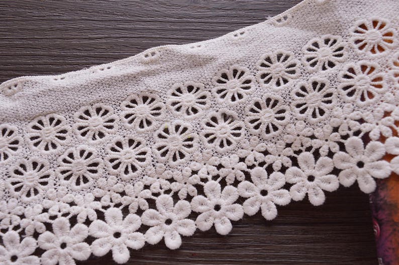 May include: White lace trim with a delicate floral pattern. The lace has a scalloped edge and is perfect for adding a touch of elegance to any project.