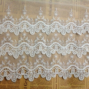 May include: White lace trim with a delicate floral pattern. The trim has a scalloped edge and is perfect for adding a touch of elegance to any project.