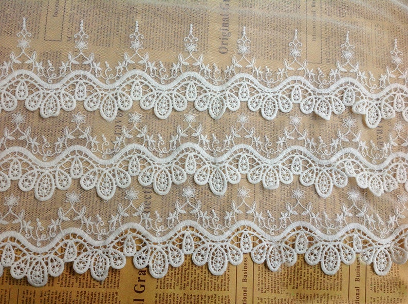 May include: White lace trim with a delicate floral pattern. The trim has a scalloped edge and is perfect for adding a touch of elegance to any project.