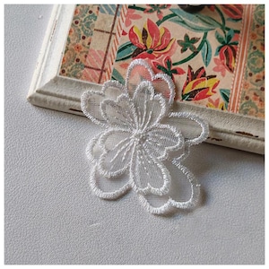 Peut inclure: Applique de fleur en dentelle blanche avec un design délicat. Cette embellissement floral est parfait pour ajouter une touche d'élégance aux vêtements, à l'artisanat ou à la décoration de la maison.