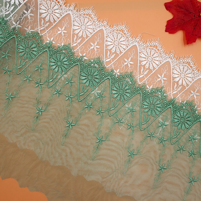 May include: White and green lace trim with a scalloped edge. The lace has a floral design with a delicate, intricate pattern.