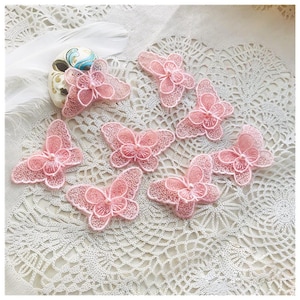 Op de afbeelding: Roze kanten vlinder applicaties. Deze delicate vlinderversieringen hebben ingewikkelde bloemendetails en zijn perfect voor knutselprojecten. De vlinders zijn ongeveer 5 cm breed.