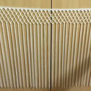 以下が含まれることがあります： 結び目のネットデザインが施された白いフリンジトリム。フリンジの長さは約5cmです。