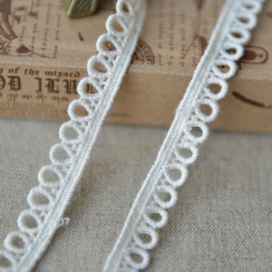 May include: White cotton lace trim with a scalloped edge and small loops. The trim is approximately 1/2 inch wide.