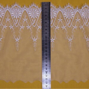 May include: White lace trim with a scalloped edge and floral embroidery. The trim is approximately 2.5 inches wide.
