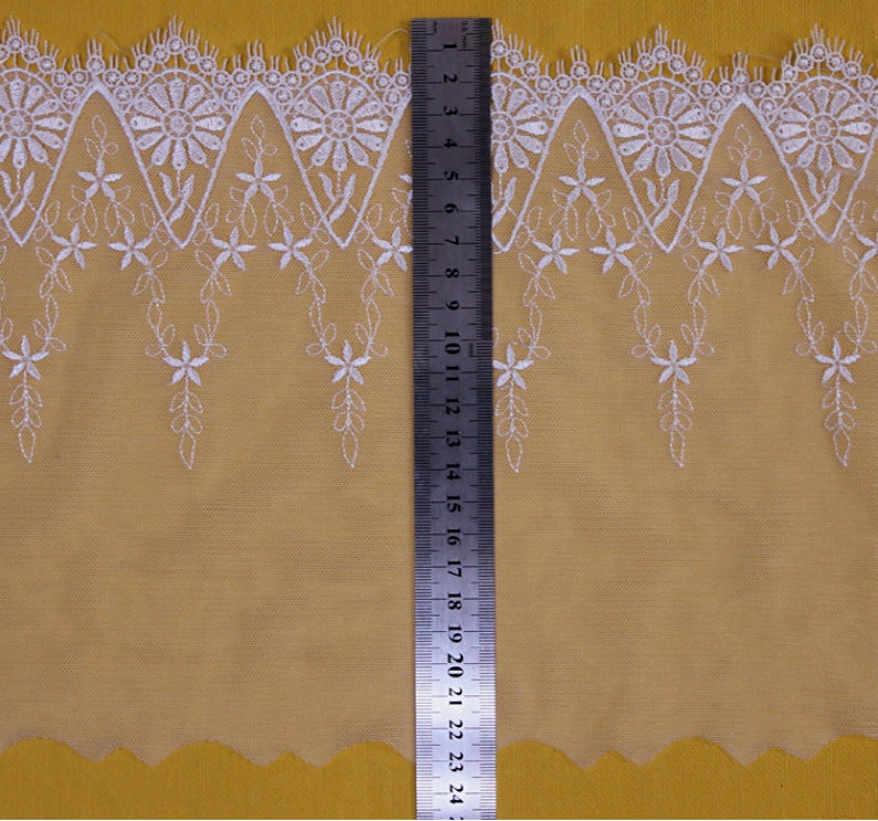 May include: White lace trim with a scalloped edge and floral embroidery. The trim is approximately 2.5 inches wide.