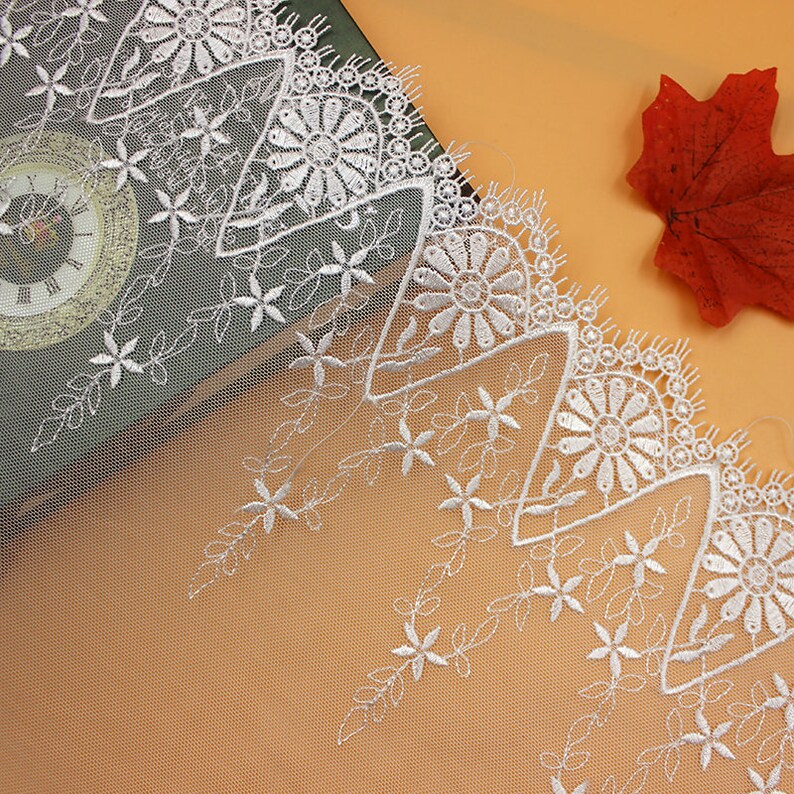 May include: White lace trim with a delicate floral pattern. The lace features a scalloped edge and a repeating design of small flowers and leaves.