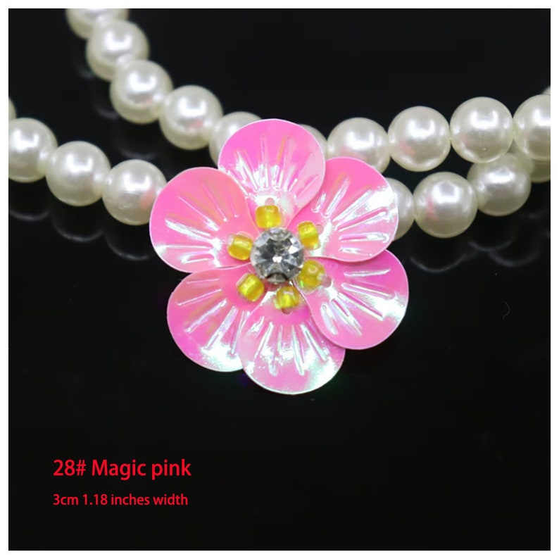 May include: A necklace featuring a strand of white faux pearls and a central pink flower embellishment. The flower has five iridescent petals, yellow seed beads, and a clear center stone. Text reads 28# Magic pink and 3cm 1.18 inches width.
