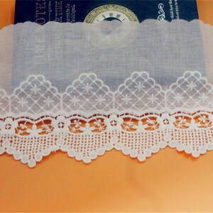 May include: White cotton lace trim with a scalloped edge and a delicate floral pattern. The lace is approximately 1 inch wide.