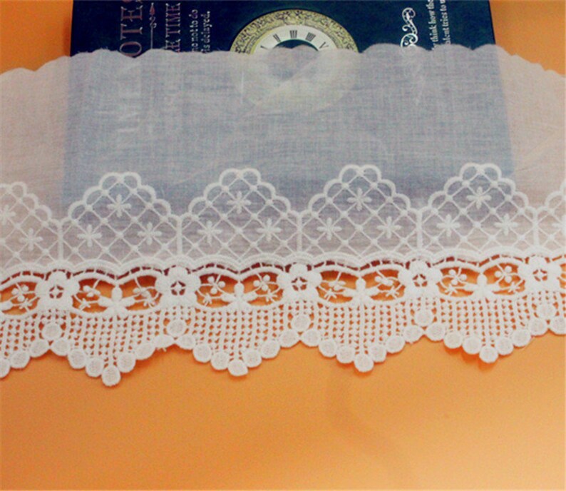May include: White cotton lace trim with a scalloped edge and a delicate floral pattern. The lace is approximately 1 inch wide.