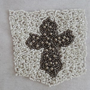 May include: A white and silver beaded cross applique. The cross is made of silver beads and is surrounded by white beads.