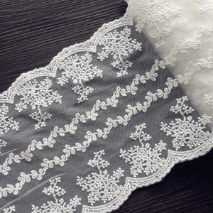 May include: White lace trim with a delicate floral and snowflake design. The lace is soft and sheer, with a scalloped edge.