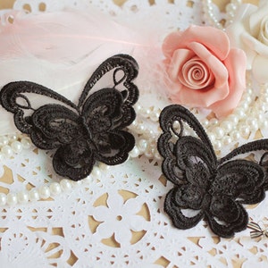 Può includere: Due applicazioni di farfalla in pizzo nero su uno sfondo di pizzo bianco. Le farfalle sono delicate e intricate, con un design dettagliato.