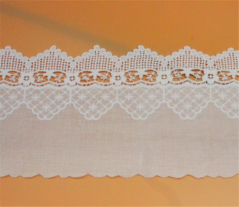 May include: White cotton lace trim with a scalloped edge and a delicate floral pattern. The lace is approximately 1 inch wide.