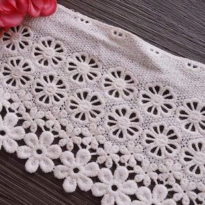 May include: White lace trim with a scalloped edge and a delicate floral pattern. The lace has a repeating design of small flowers and circles.